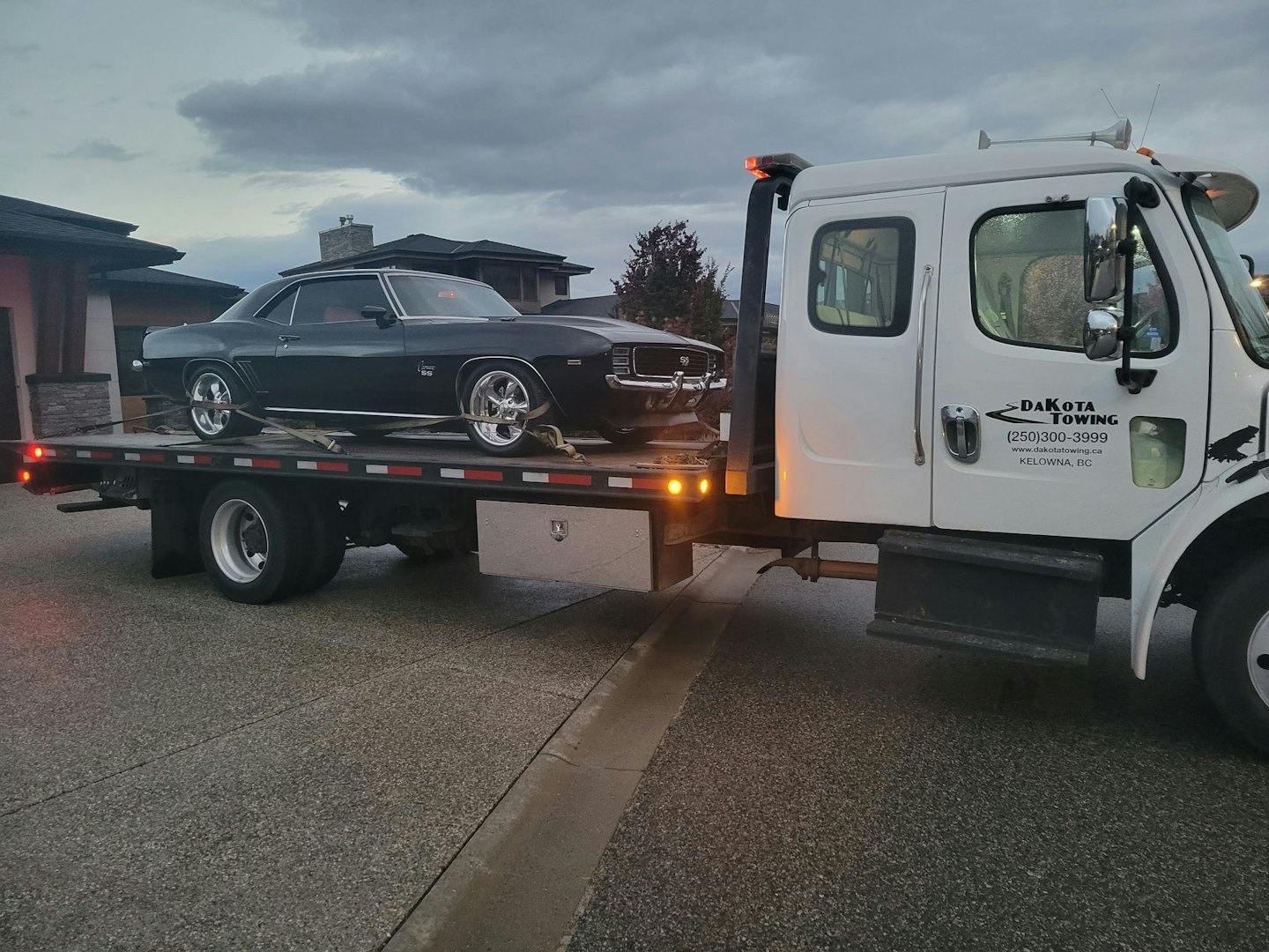 Samochód pomocy drogowej przewożący klasycznego Chevroleta Camaro ulicą.