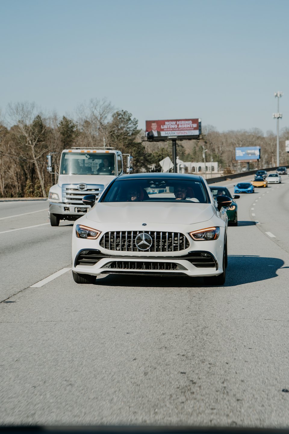 Biały sedan Mercedesa jedzie w stronę widza po autostradzie z pomocą drogową.